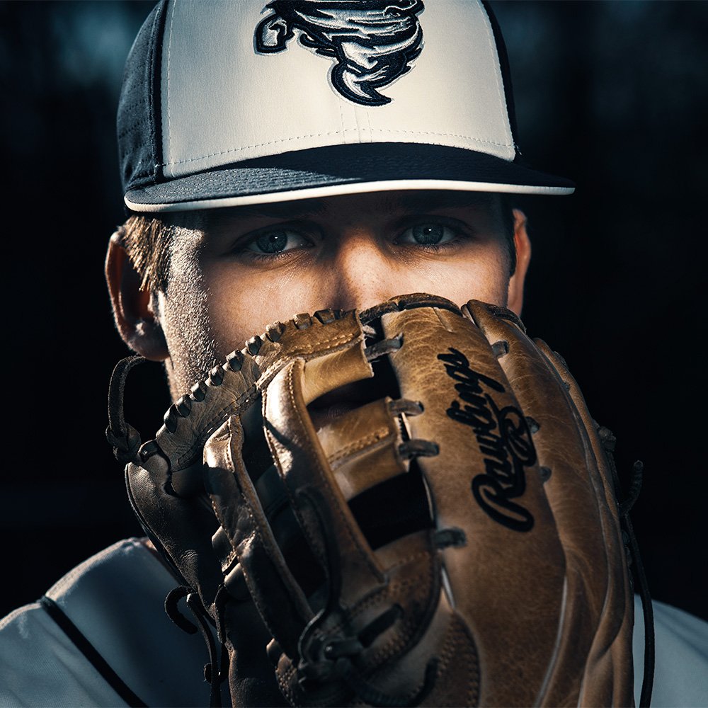 Don Evans Photography in Greensboro high school senior wearing his baseball uniform holds his mitt to his face during his senior picture photo session