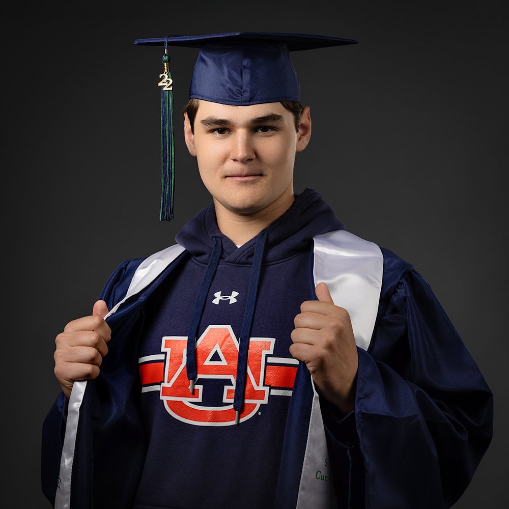 Don Evans Photography in Greensboro high school senior wearing his blue cap and gown opens his gown to reveal his college during his fall graduation senior picture photo session