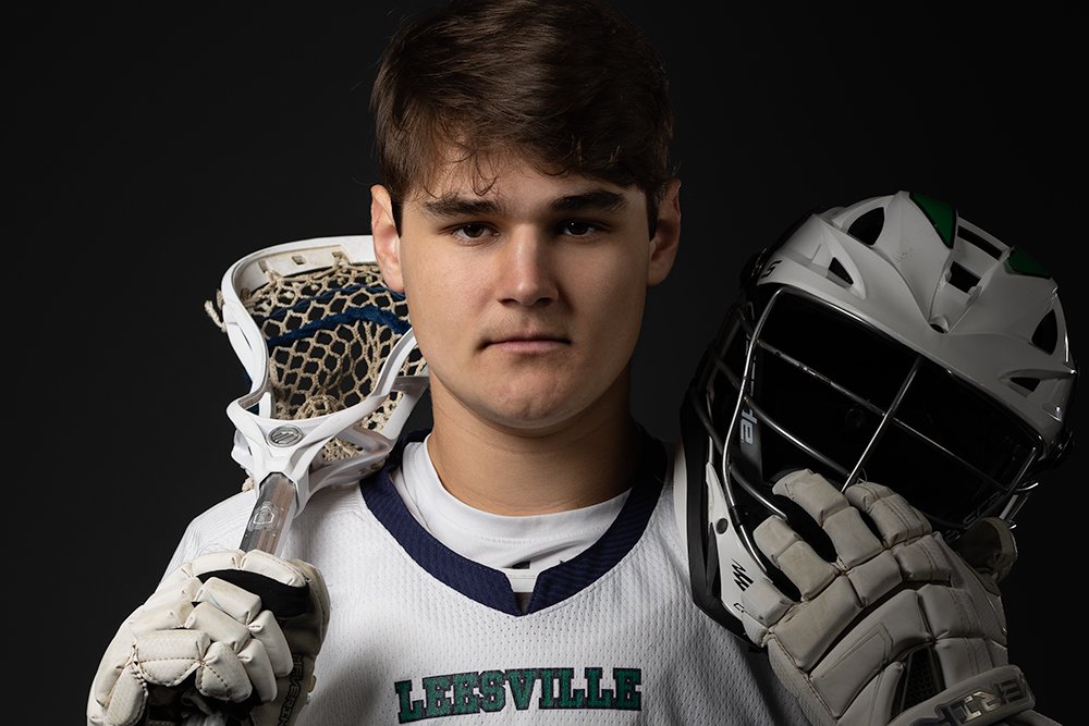 Don Evans Sports Photography in Greensboro NC Dramatic Senior Sports Portraits lacrosse player holds his stick and helmet during his senior banner photo session