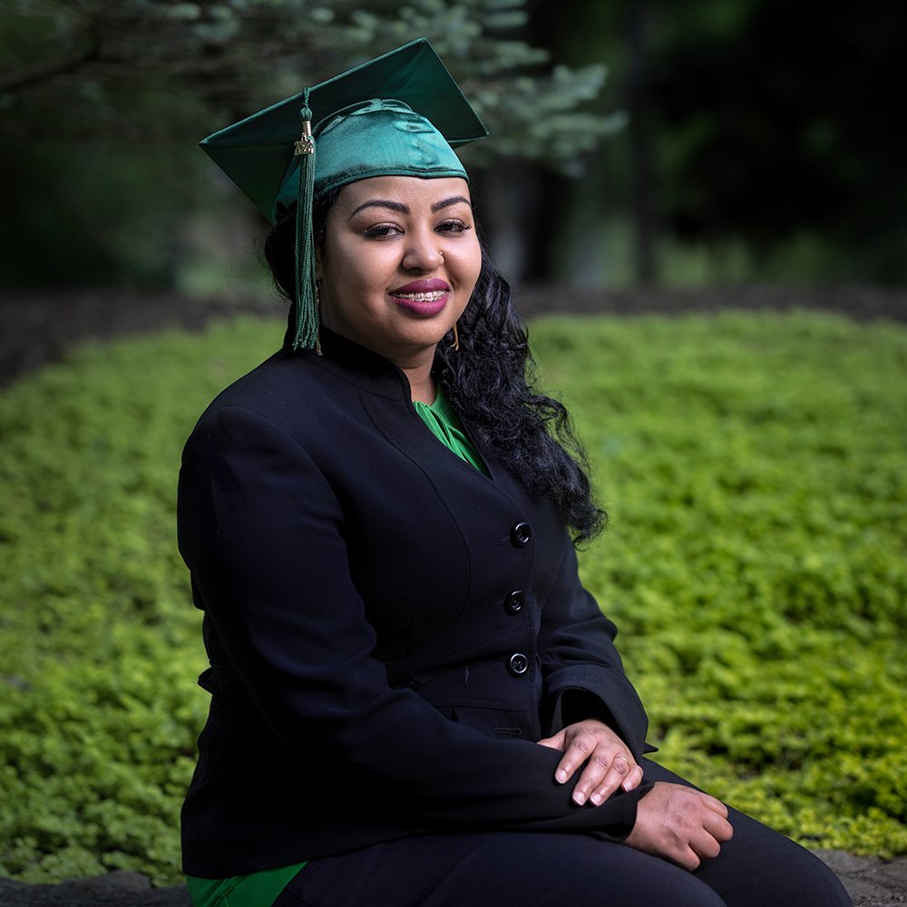 Don Evans Photography in Greensboro NC A&amp;T college grad wearing black suite and graduation cap sits in a park during her graduation senior picture photo session