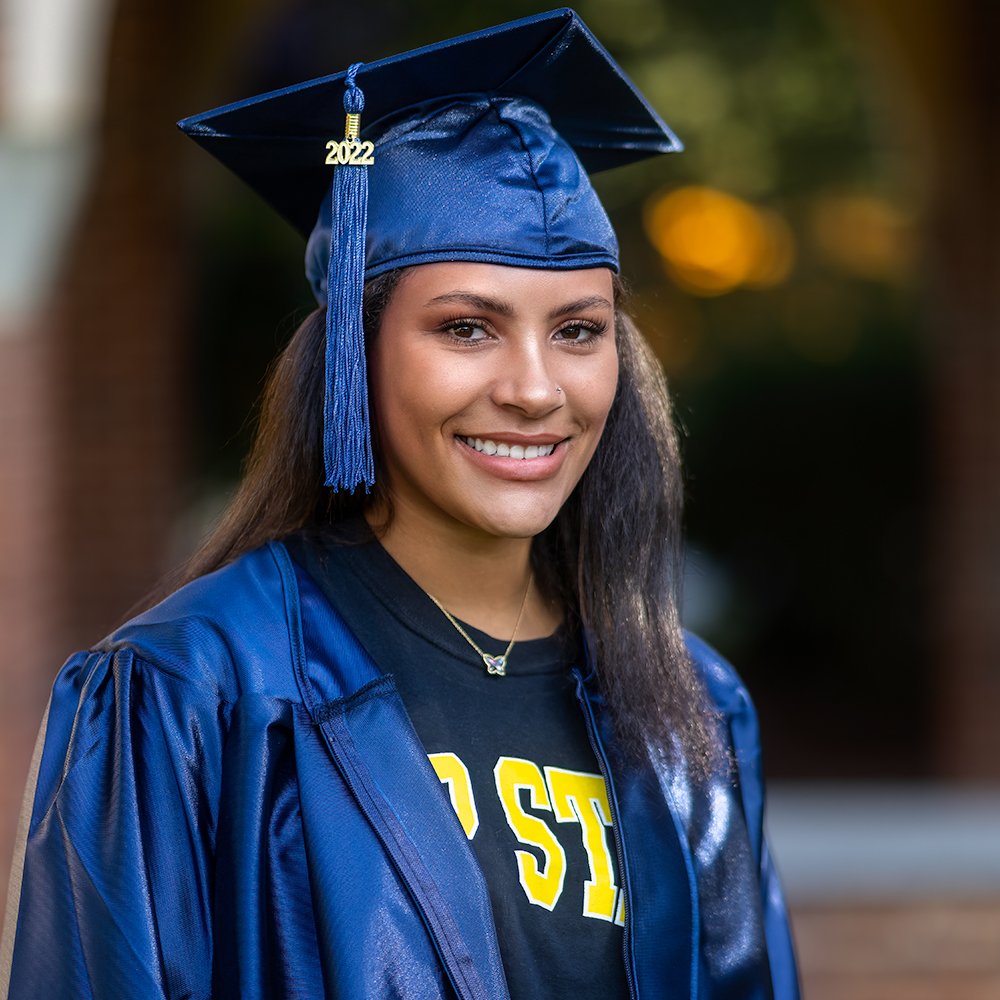 Don Evans Photography in Greensboro high school senior wearing her blue cap and gown on campus smiles at the camera during her graduation senior picture photo session