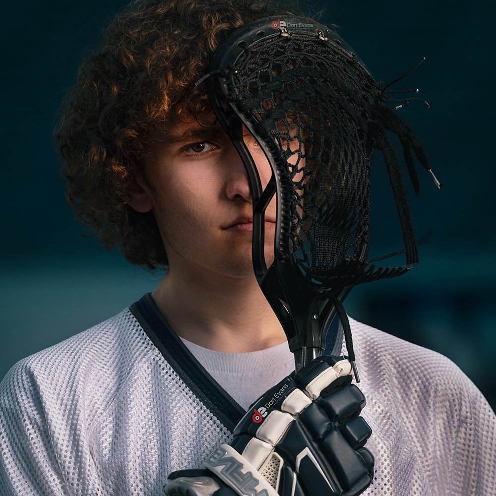 Don Evans Photography in Greensboro picture of a senior lacrosse player holding his stick up to his face during his senior pictures photo session.jpg