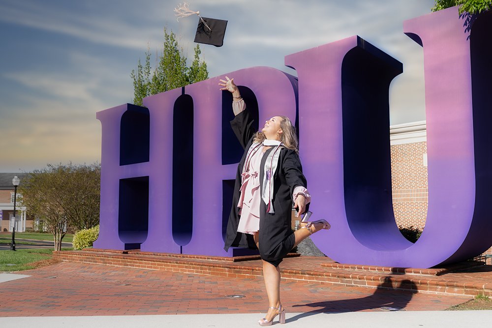 Don Evans Photography in Greensboro a High Point University college graduate in cap and gown throws her cap in the air during her senior graduation photo session