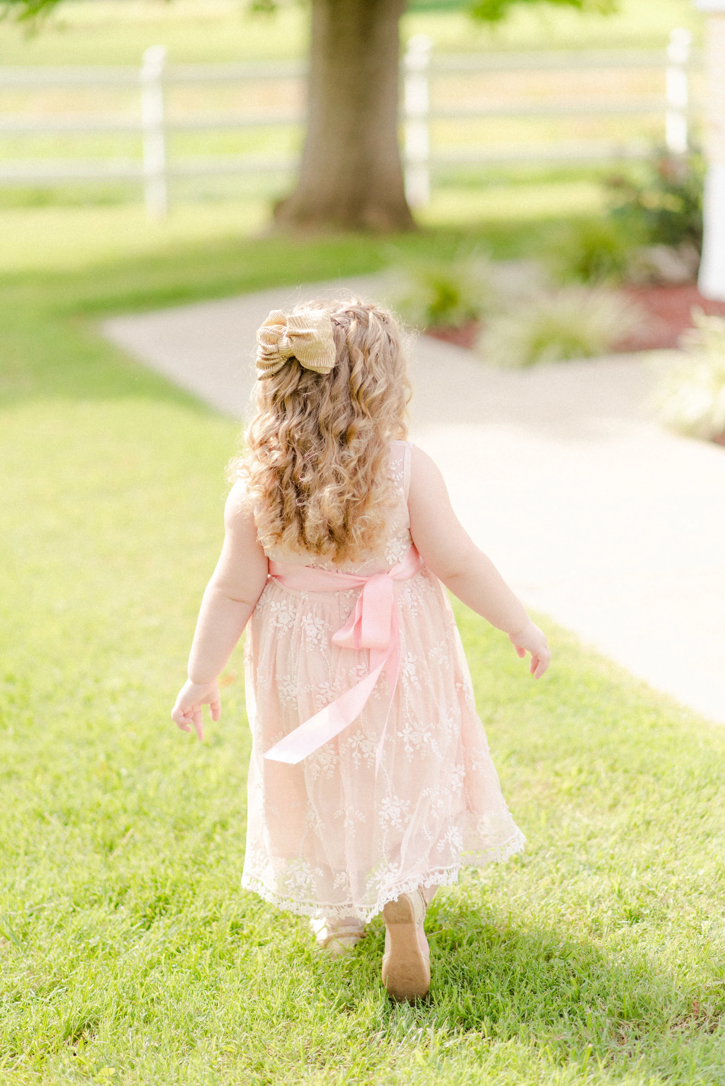 The Starns Wedding – July 2018 When I stumbled upon this photo while editing, I fell in love with it. Others may look past this image without a second thought, but I find something captivating about it. I love the hue of the grass, the delicacy of the pink dress, the dress ribbon blowing in the wind, and how she was captured mid-step. This image reminds me of the joy and safety of childhood.