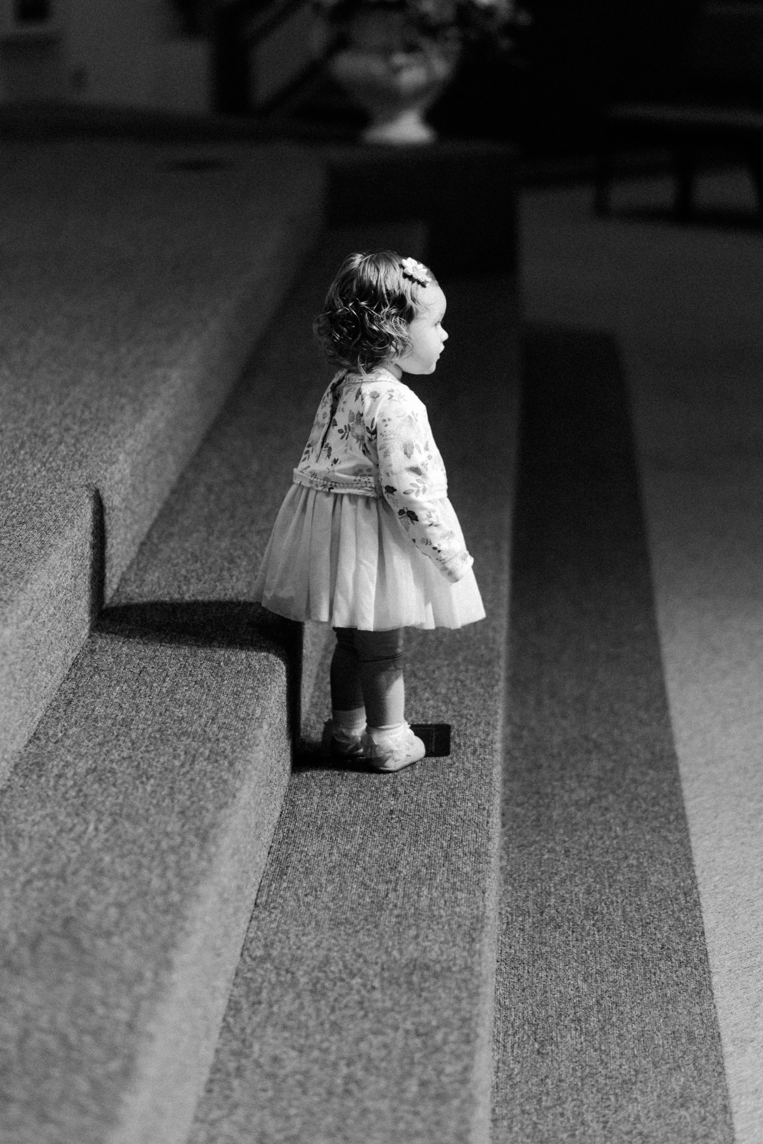 The Richards Wedding - February 2018 Once again, the moments right before a wedding ceremony are invigorating to capture. “You never know what you’re gonna get!” At this particular wedding, this sweet little gal kept making her way up to the front of the church to climb up and down the steps, over and over. It was super cute, and she really entertained us all while we waited for the ceremony to begin. I think what I enjoy most about this picture are the directional lines and pattern(s) that were created by the steps and the shadows casted by the lights above. The eye is drawn directly to the little girl, and her expression is inquisitive. It makes you wonder what she was thinking.
