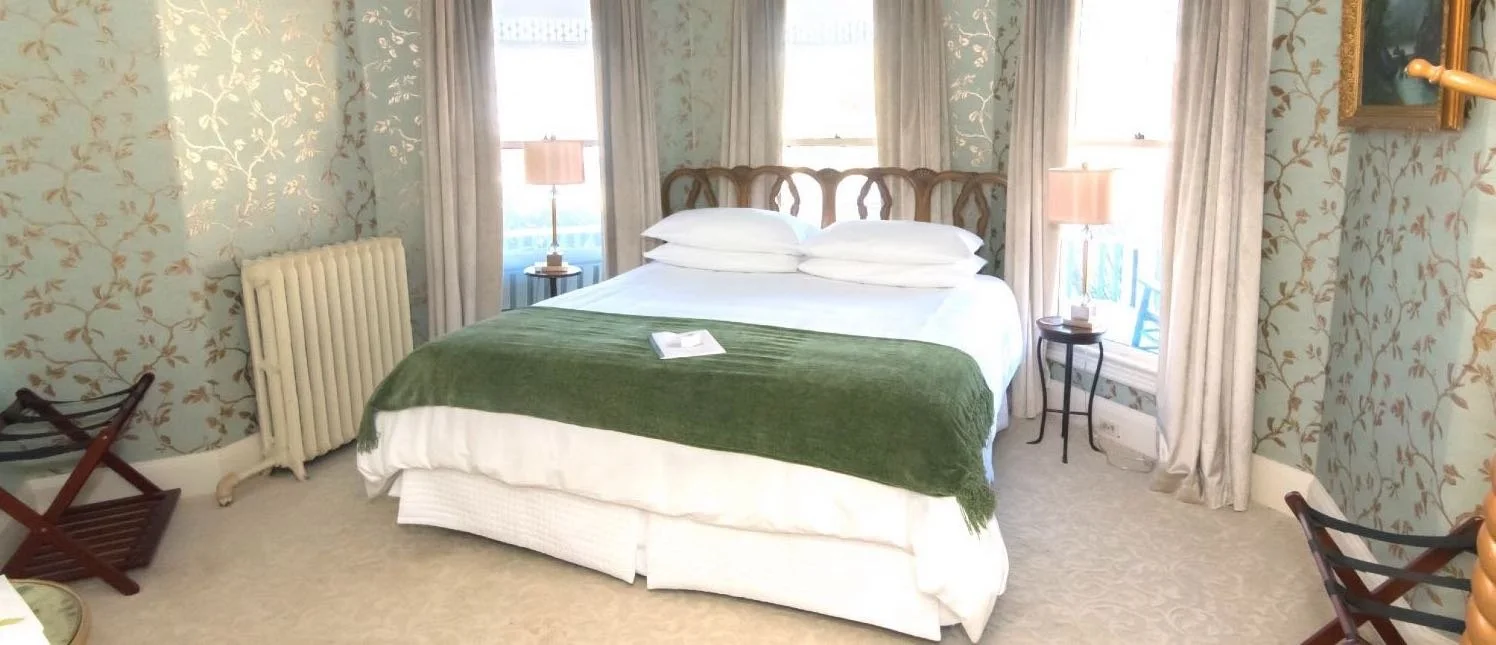 A bedroom with a bed, nightstands, lamps, and windows with curtains.