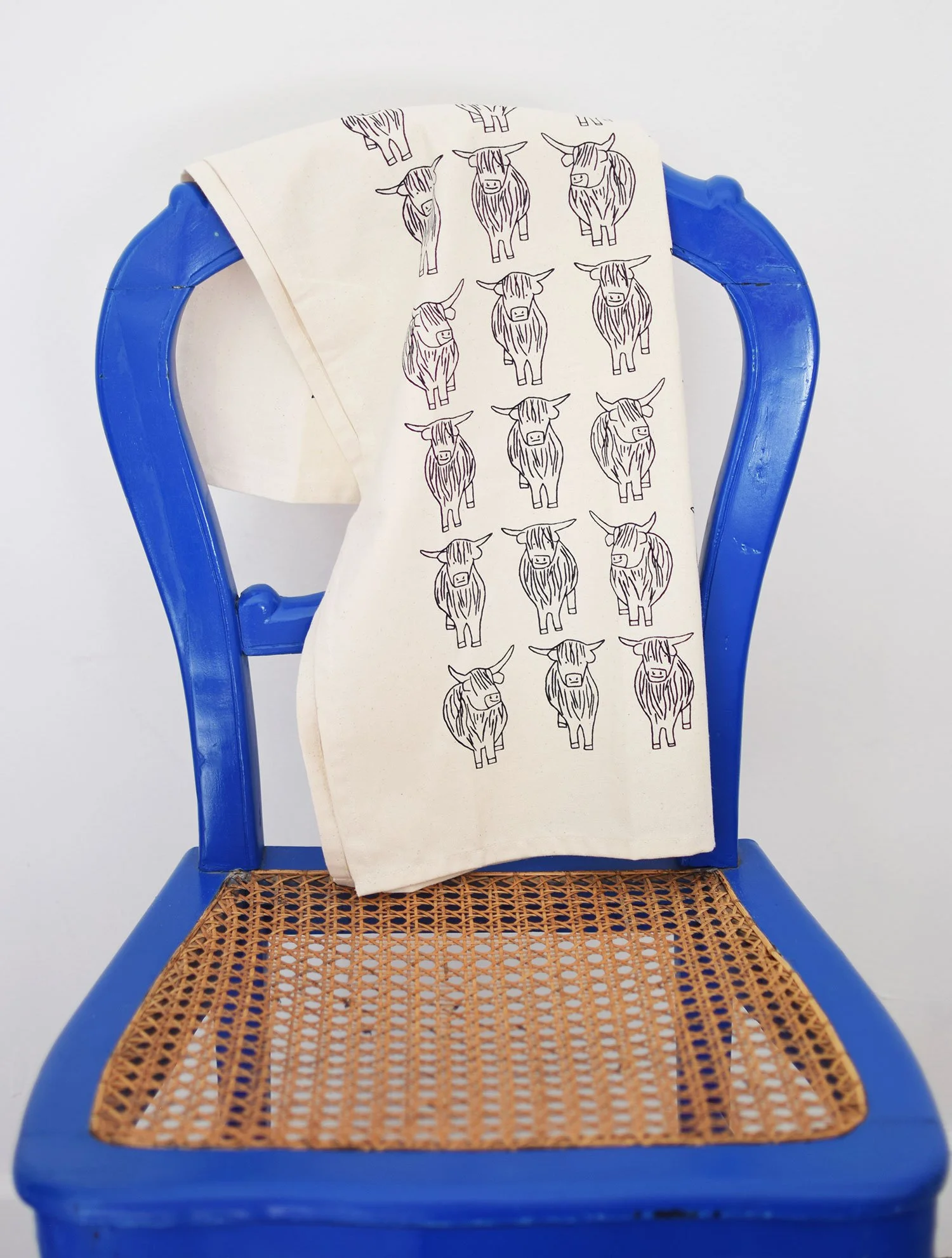 Highland cows tea towel designed by local Edinburgh artist Sally Fisher blue chair