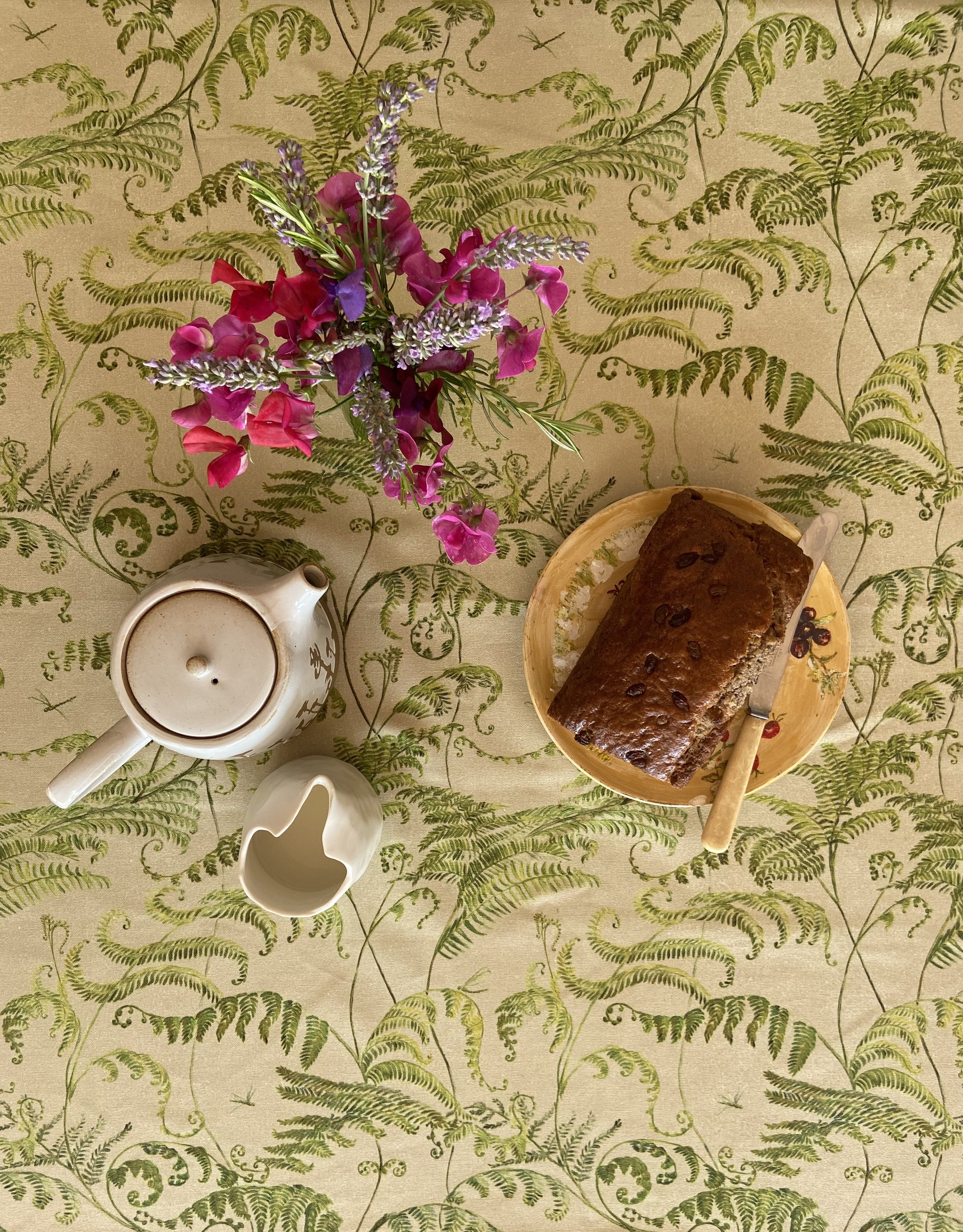 Botanical fern table cloth on sage green background with sweet pea flowers cake and tea pot