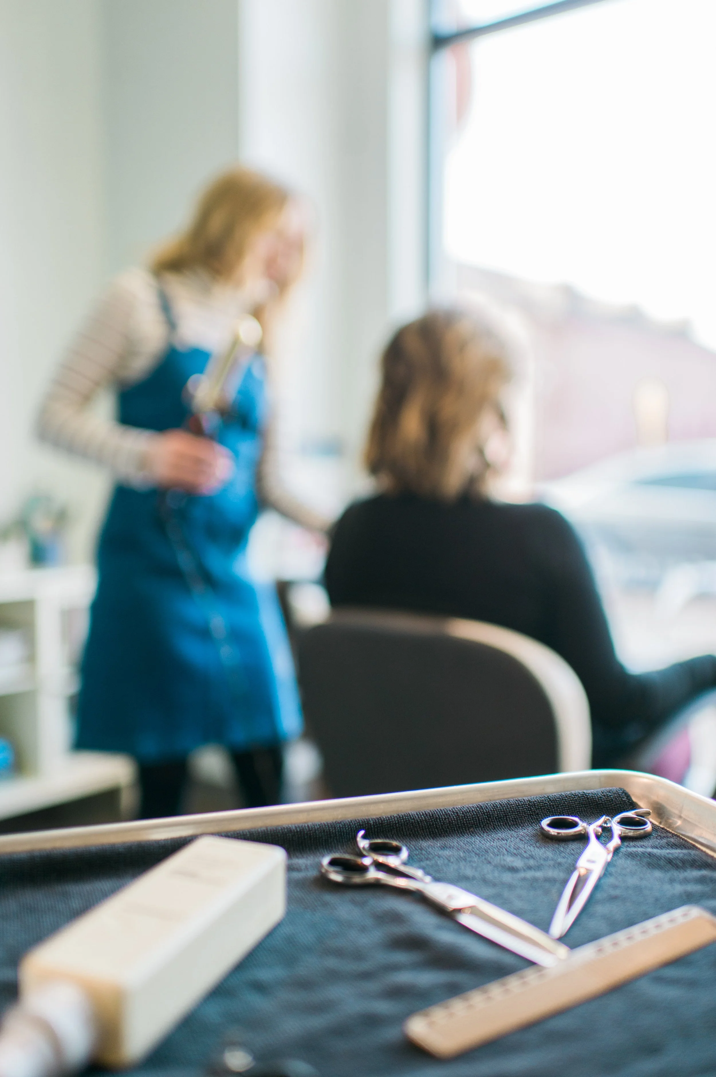 Hair styling tools on a tray with a stylist working with a client in a modern Carmel, Indiana hair studio.