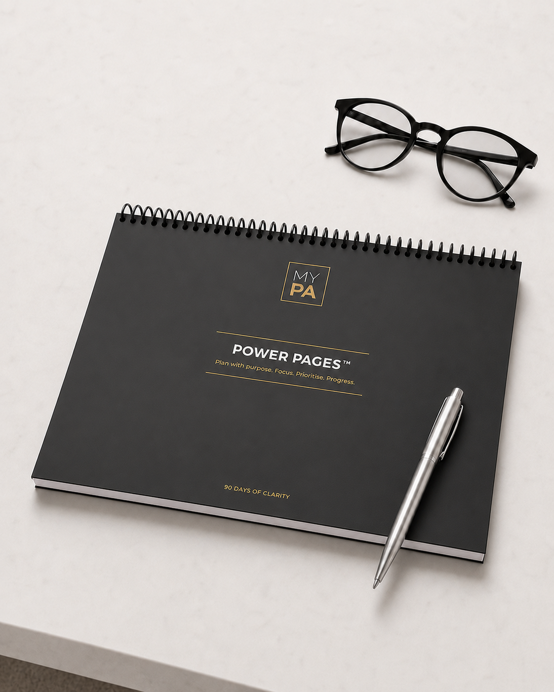 Power Pages Daily planning pad, black and gold cover, on a desk with coffee, watch and glasses