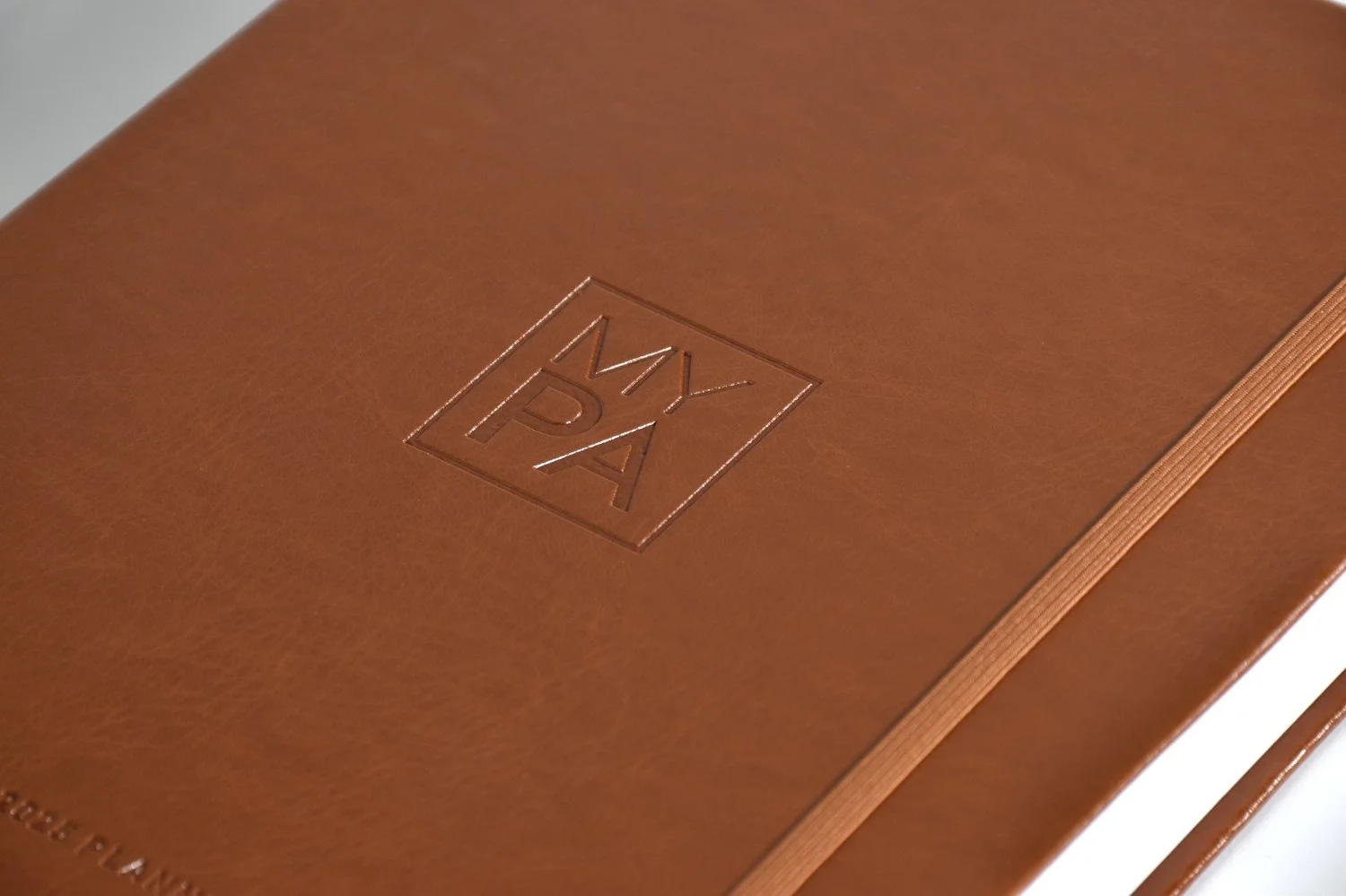 Close-up of the debossed MY PA logo on the tan vegan leather cover
