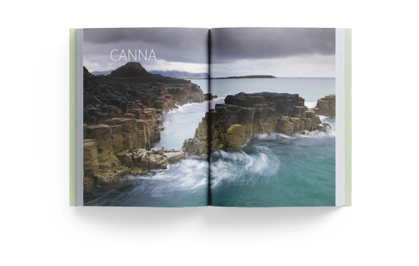 Open book showing a scenic photograph of rocky coastline with ocean waves and cloudy sky, with the word 'CANNA' on the left page.