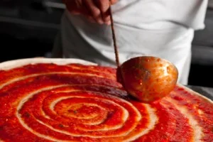 Chef using ladle to spread sauce on a pizza