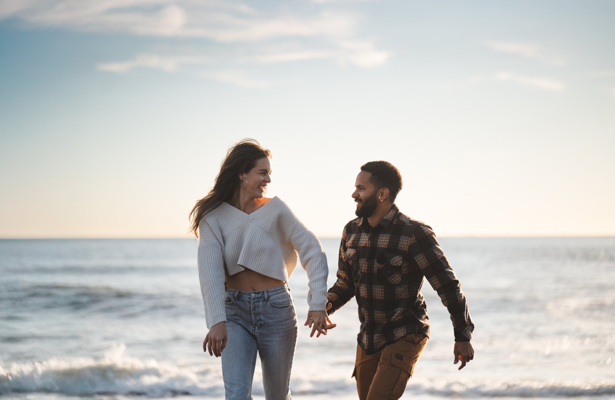 Couple holds hands and smile at each other while running at Rodeo Beach