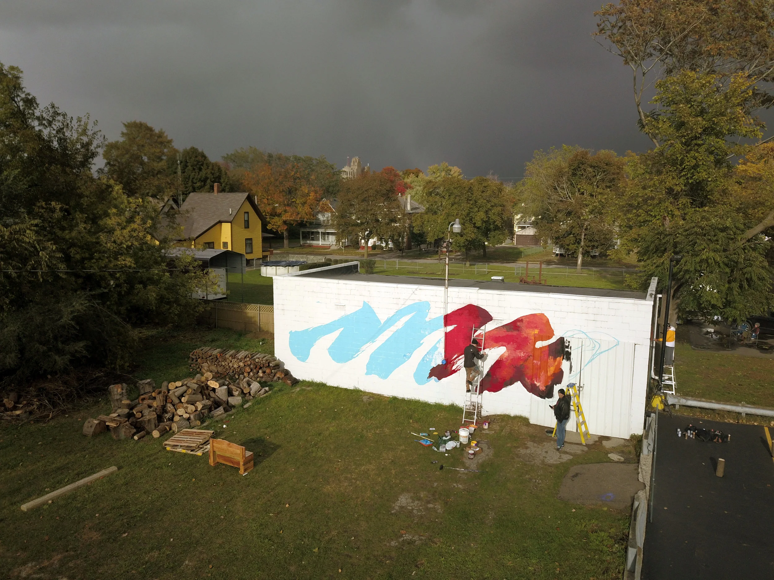 storm clouds cast a trace rainbow over the flint skyline as meggs continues his piece. flint public art project executive director joe schipani regards with approval.