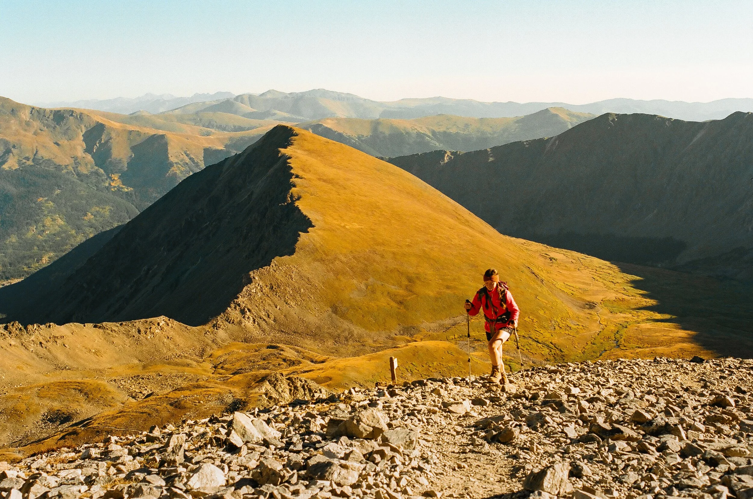 A person hiking on a rocky mountain trail with mountains and hills in the background during daytime.
