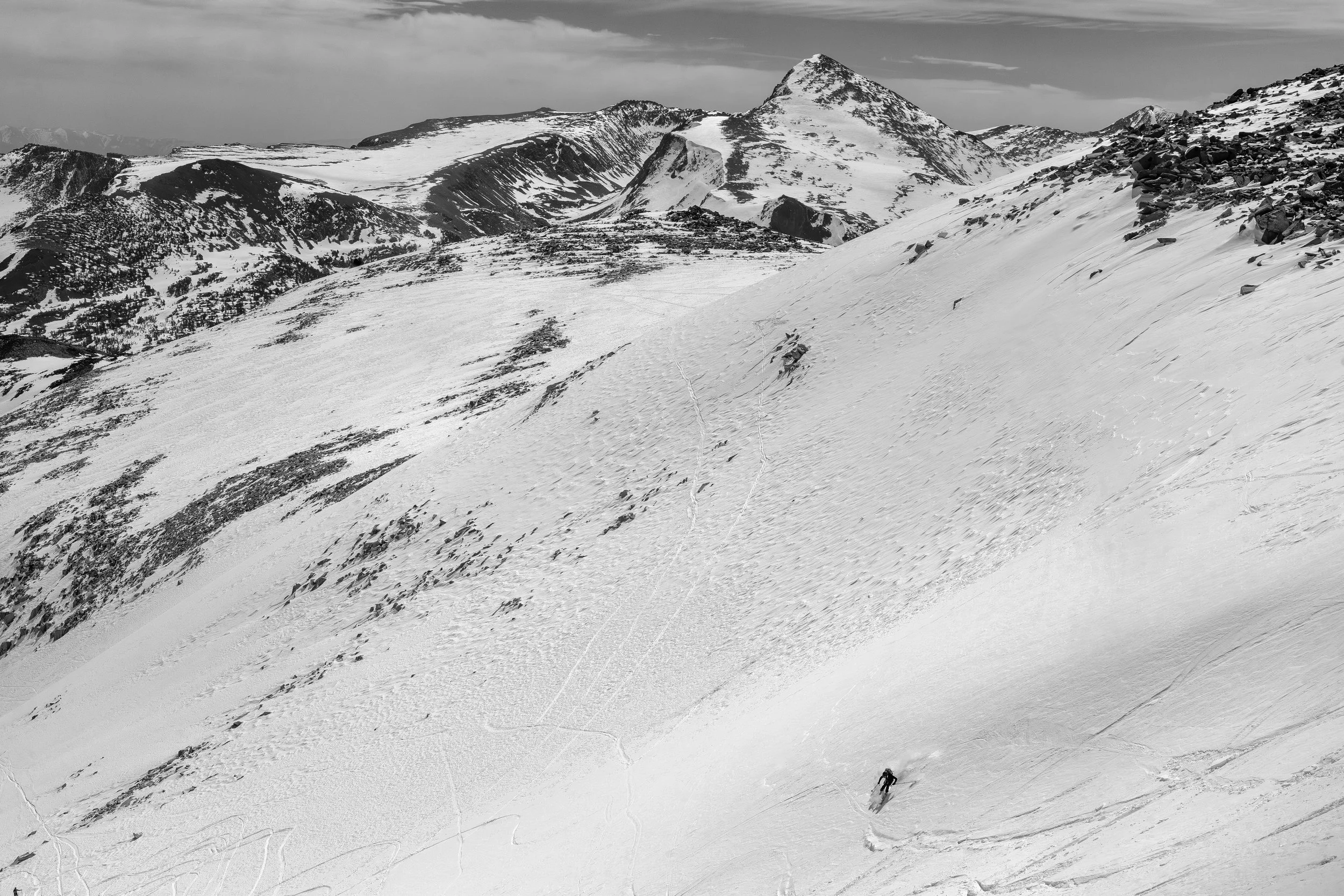 A snow-covered mountain landscape with a skier descending the slope and visible ski tracks in the snow.