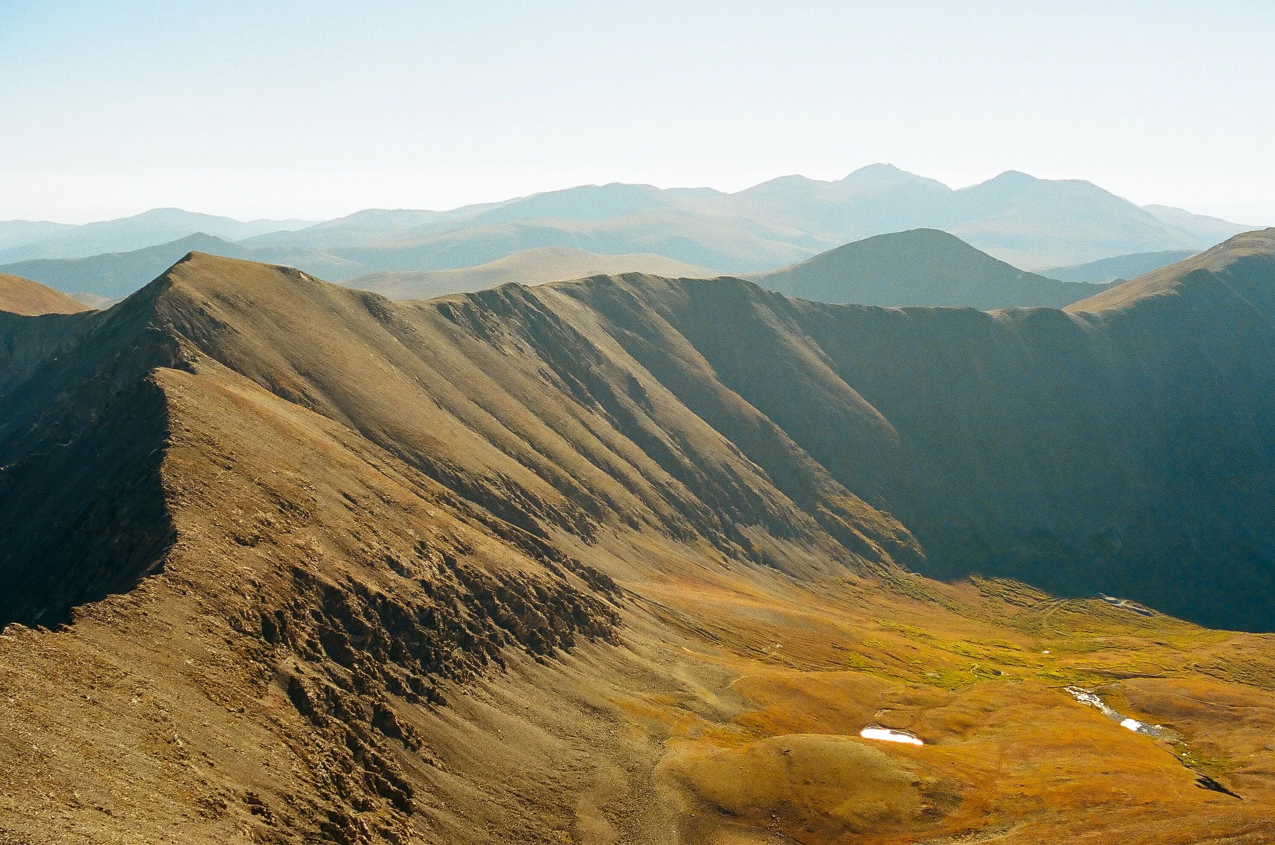 Panoramic view of a mountain range with rolling hills and valleys, featuring rugged terrain and sparse vegetation.