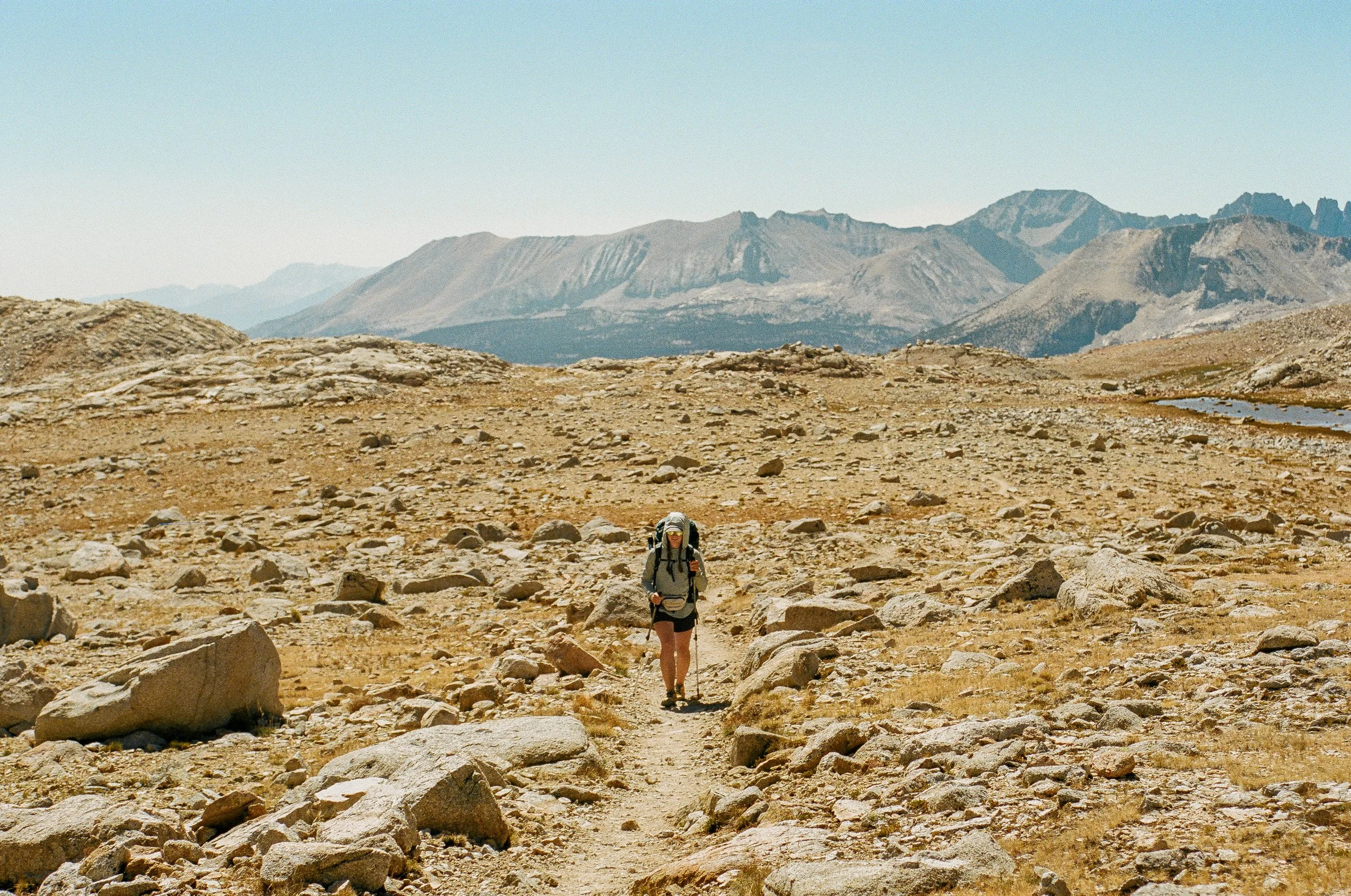 Hiker walking on rocky desert terrain with mountains in the background.