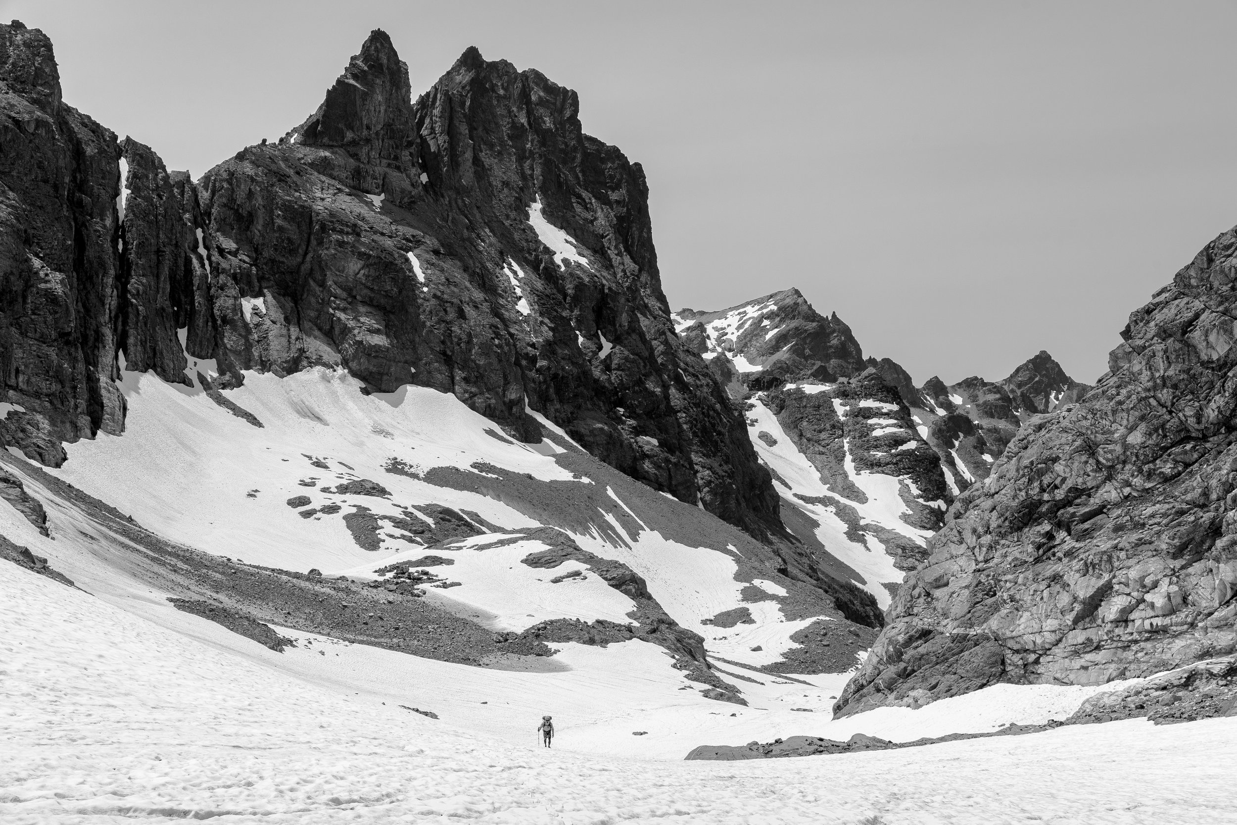 Black and white photo of snow-covered mountains with a lone hiker in the foreground.