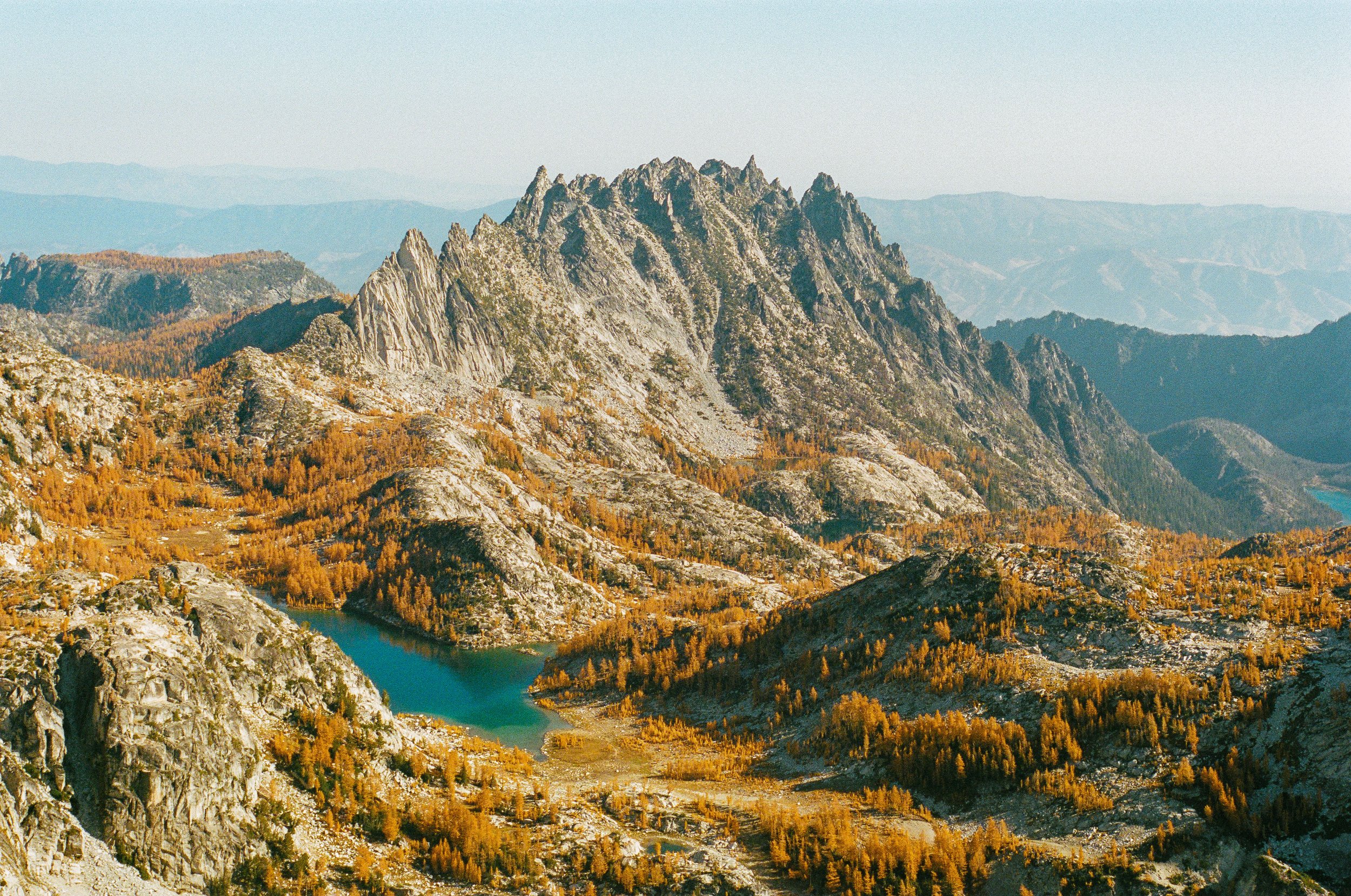 Scenic view of rugged mountains with rocky peaks, an alpine lake with turquoise waters, and autumn-colored trees in a mountainous landscape.