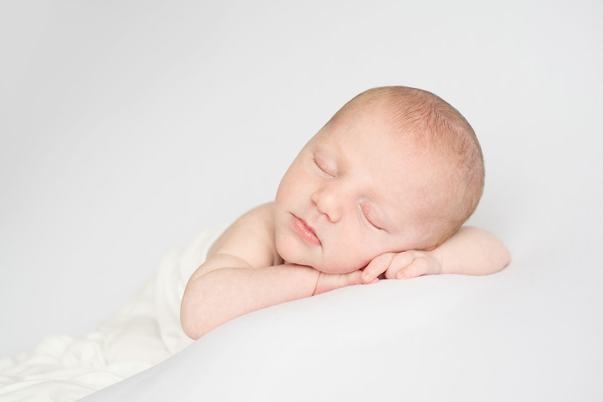  Newborn baby in white sleeping on a beanbag in a photographer's studio 