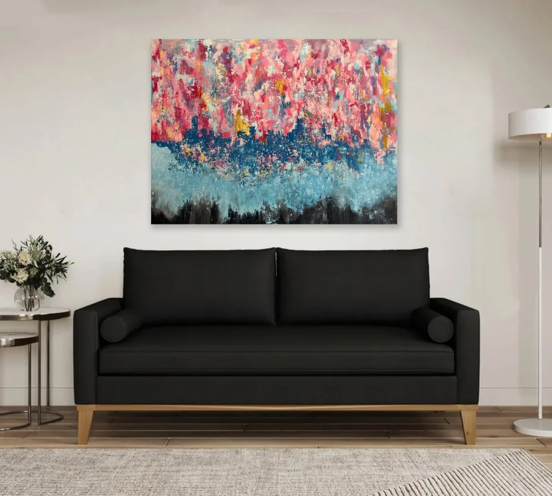 Living room with a charcoal gray sofa, a side table with a flower arrangement, a floor lamp, and an abstract painting with pink, blue, yellow, and black colors hanging on a white wall.