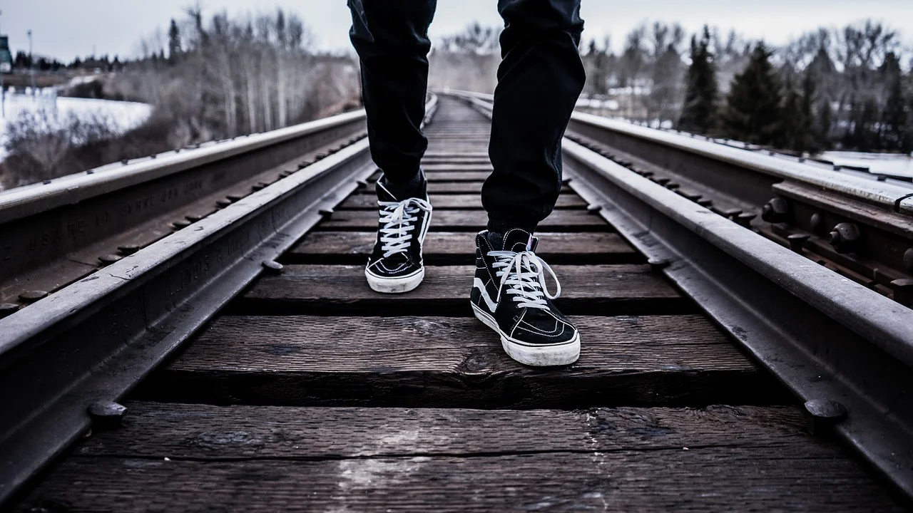Focus on a man’s shoes as he walks down railroad tracks