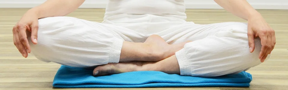 Man in White Sits Cross-Legged on Mat While Meditating
