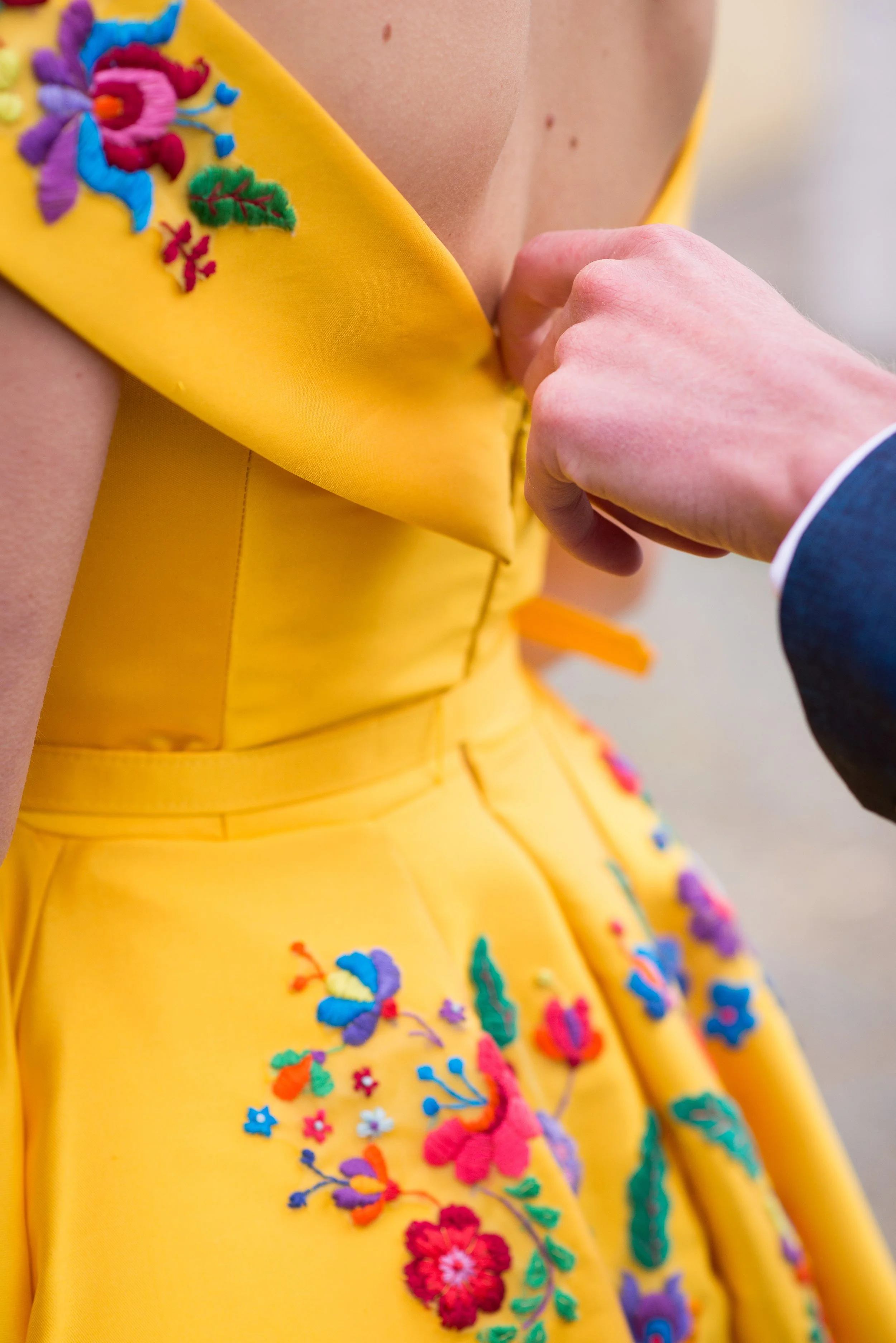  the back details of a bright yellow wedding dress embroidered with brightly coloured folky floral design. 