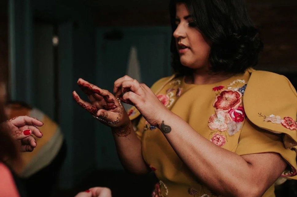  A indian bride wears a mustard Yelloe wedding dress with pink embroidered flowers on the shoulders, she inspects the henna on her hands 