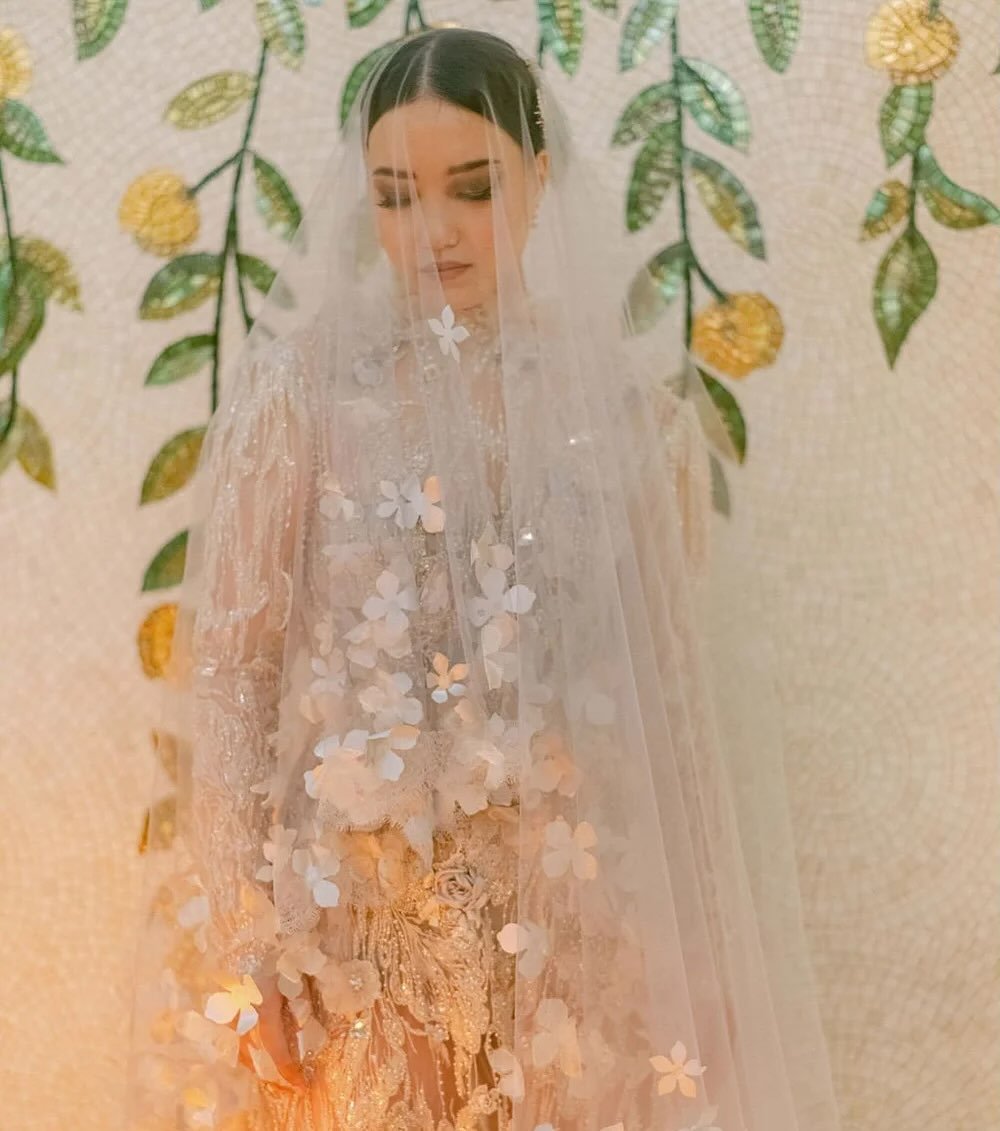 Sheer embroidered lace traced with hand-appliqu&eacute;d petals, crystals and sparkling motifs , metallic organza frills, and a veil that becomes part of the dress itself. Delicacy, texture, sparkle, and silhouette.

Every element is cut, placed, and
