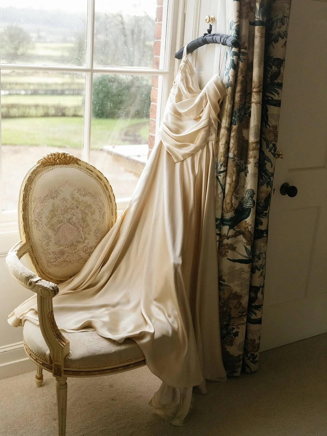 Golden ivory satin, draped by hand. The grain of the fabric leads the design, folds falling into a soft cowl, a sculpted waist, and a skirt that moves fluidly. In motion, it catches the light like poured gold; at rest, it settles into something almos