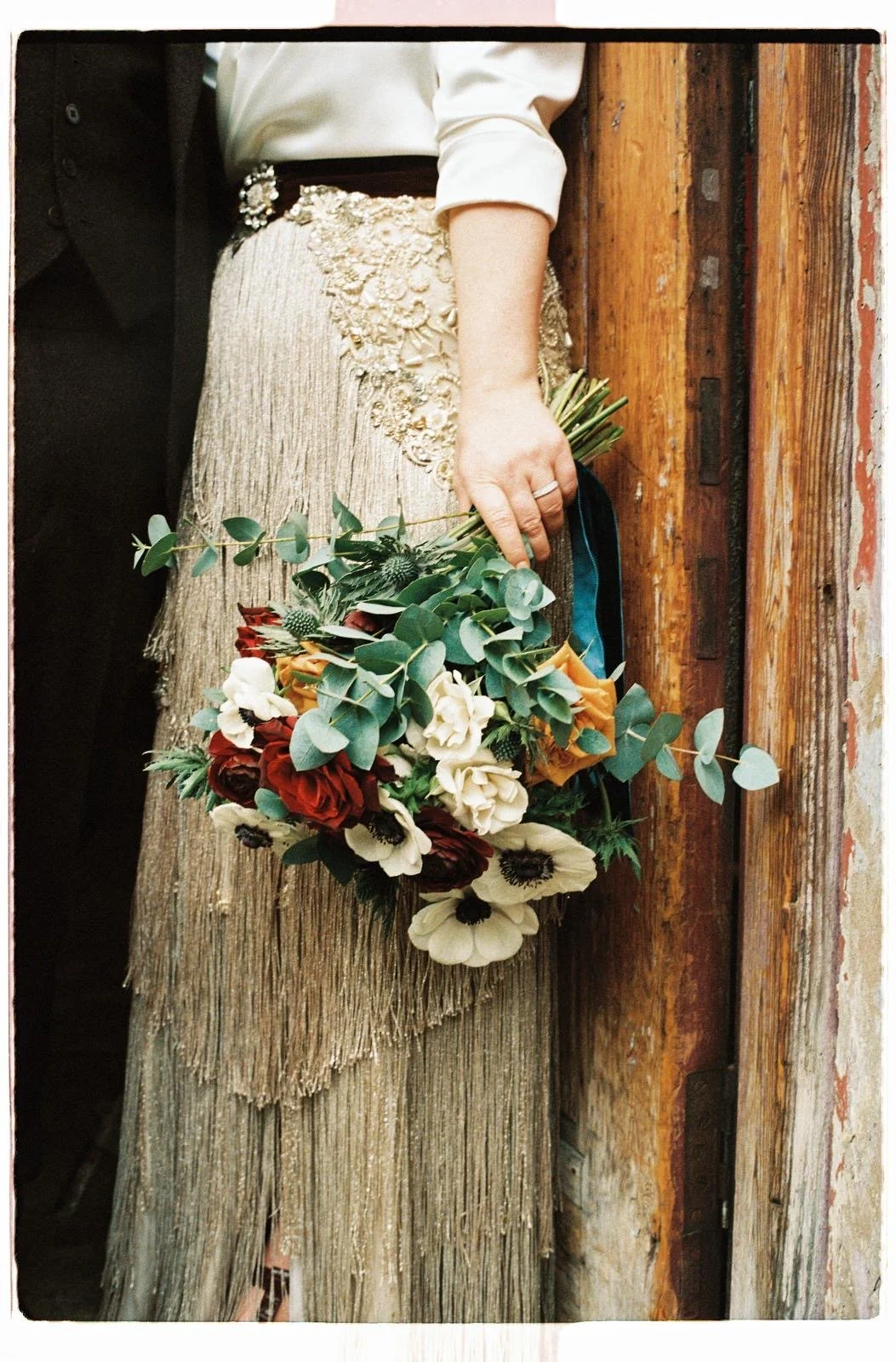 focus on the skirt of a bridal dress. the skirt is made. from gold metallic fringing, layered and cut at different lengths and angles. embellished with lace, beads and pearls, by wilden London