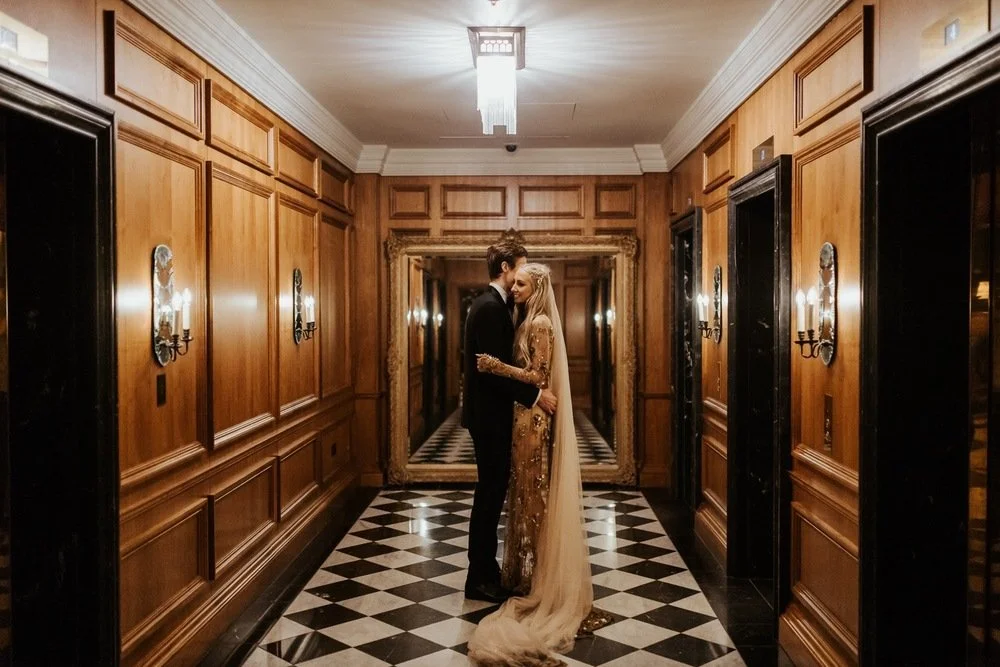 a bride and groom embrace at the ned in london, the bride wears a gold dress and veil.