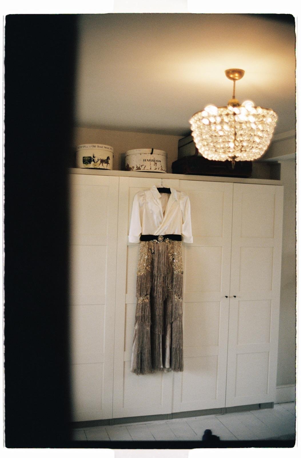a bespoke wedding dress hangs in the brides suite before the wedding in London. the top is an ivory silk blouse, and the skirt is made in gold fringe. Bespoke bridal by Wilden london.