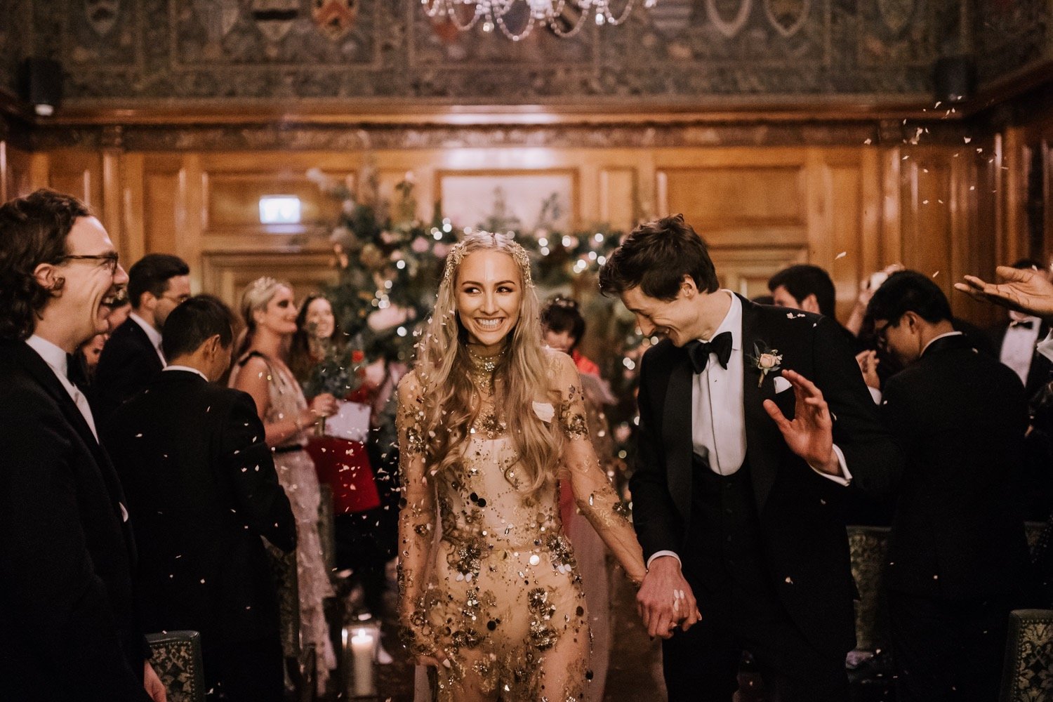 A bride and groom leave the ceremony after saying I Do, the bride wears a sheer gold embellished wedding dress
