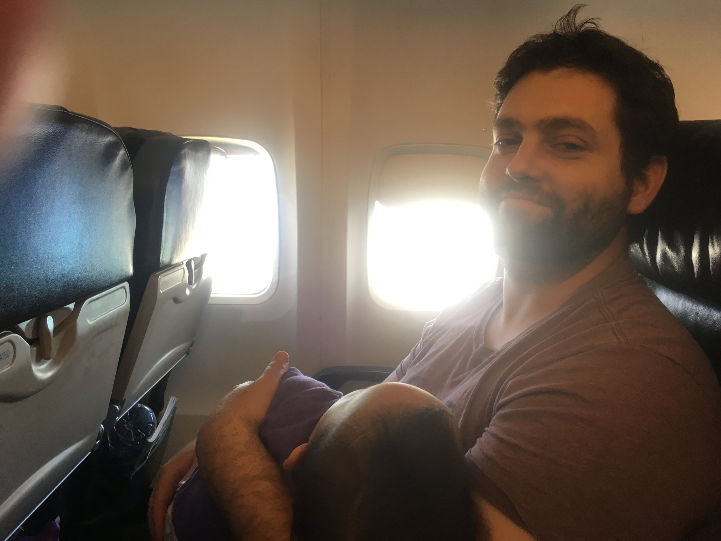 Photo by Brendan Smith. Portrait of Aaron holding his youngest daughter finally asleep, with only a half hour of the flight to go.