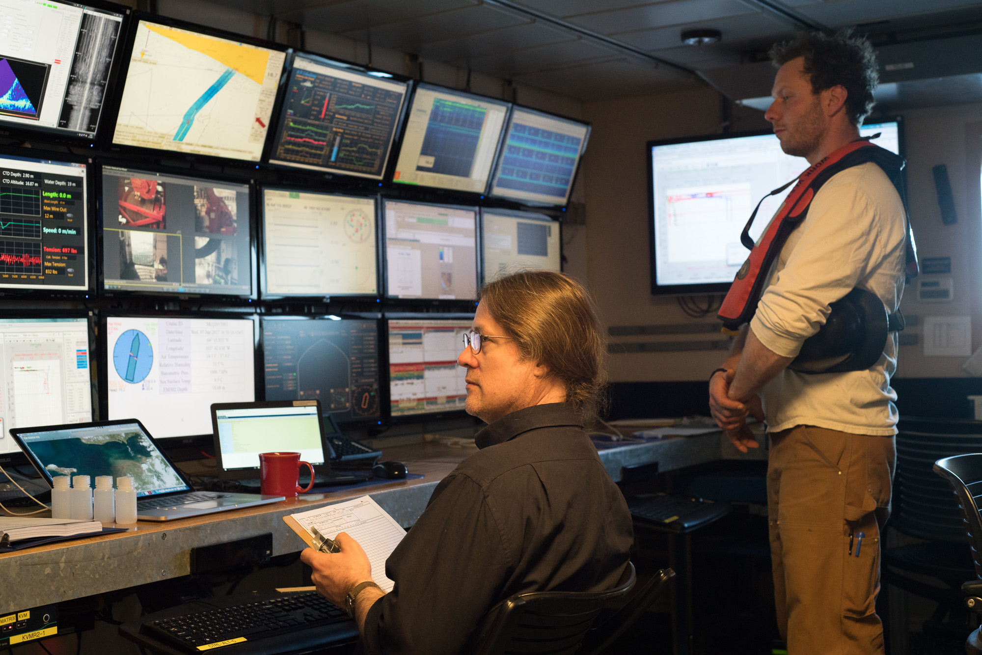 Chief Scientist Seth operates the CTD rosette from the computer lab while Ethan, one of R/V Sikuliaq 's marine technicians, oversees its operation.