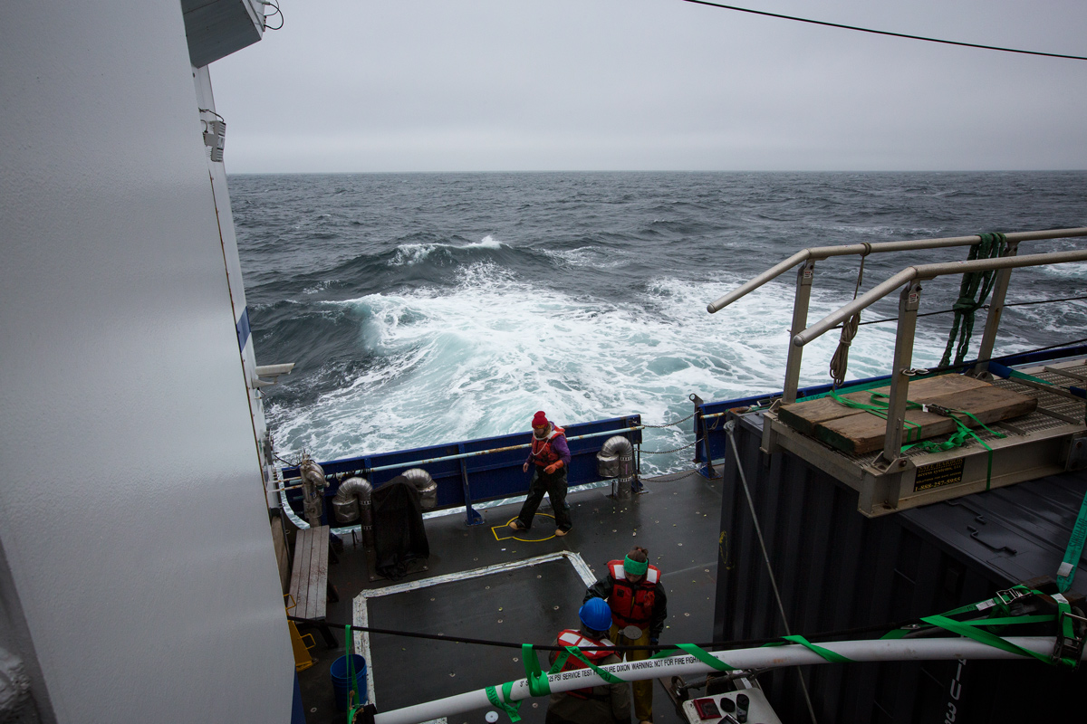 Sediment crew (Jessica Pretty and Sarah Seabrook) along with Community Observer, Opik Ahkinga, processing a recent sediment core amid a tempestuous sea. Photo credit: Brendan Smith