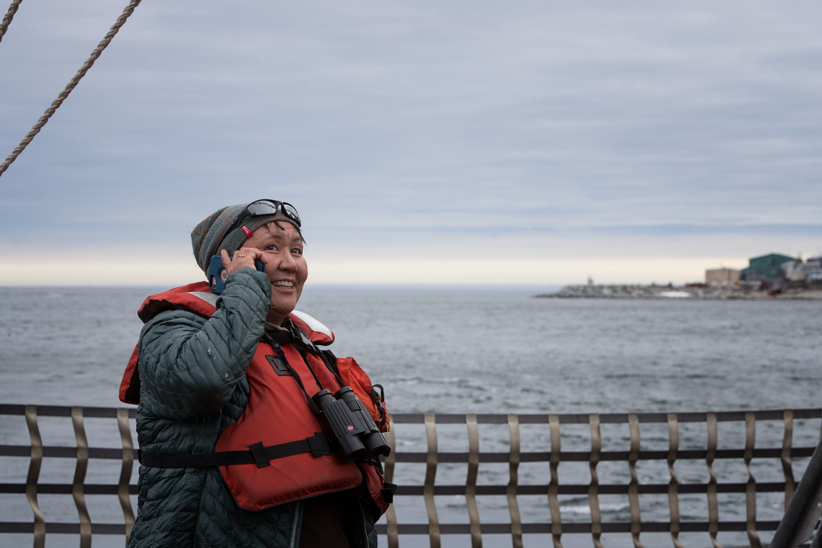 Opik using the the rare opportunity to call her dad with cellular service. Little Diomede is in the background. Her dog was waiting by the beach. Photo credit: Brendan Smith