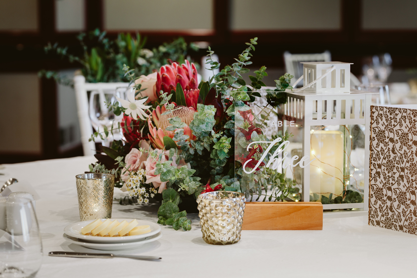 Wedding flowers and centrepieces. Australian natives and pink roses with acrylic table numbers, gold candles and fairy lights