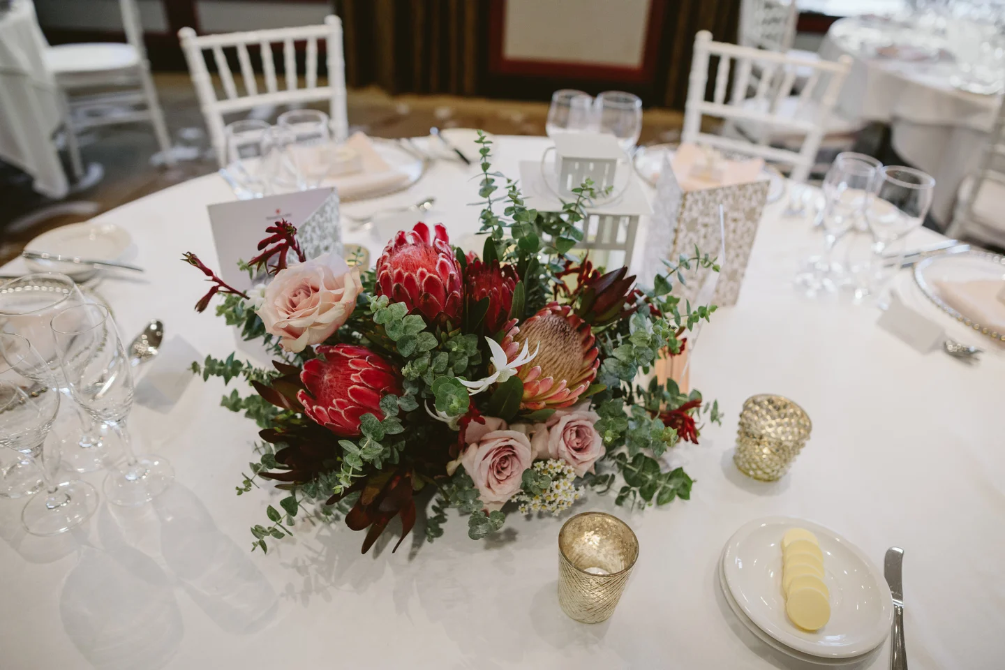 Wedding flowers and centrepieces. Australian natives and pink roses with acrylic table numbers, gold candles and fairy lights