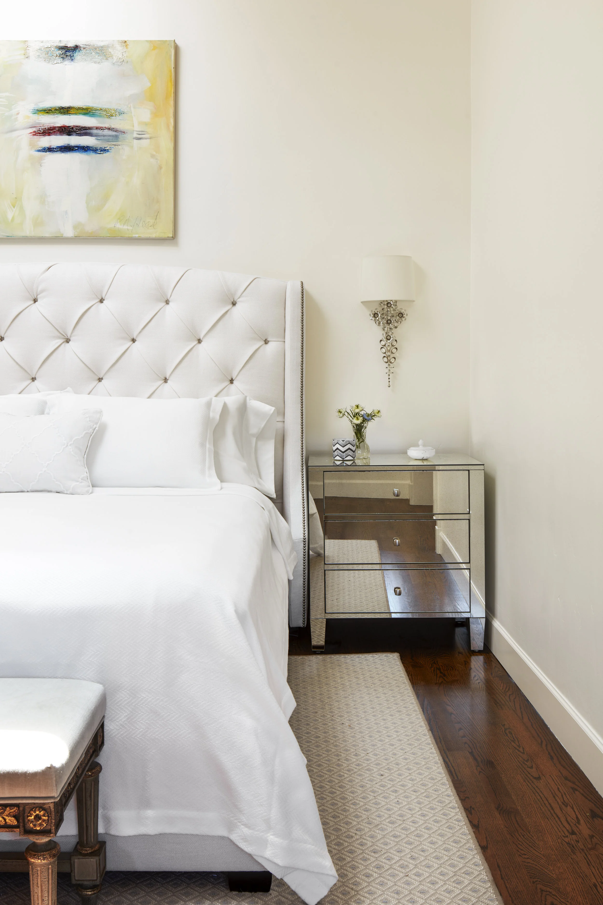 A beloved piece of the client hangs above the headboard in an all white room.