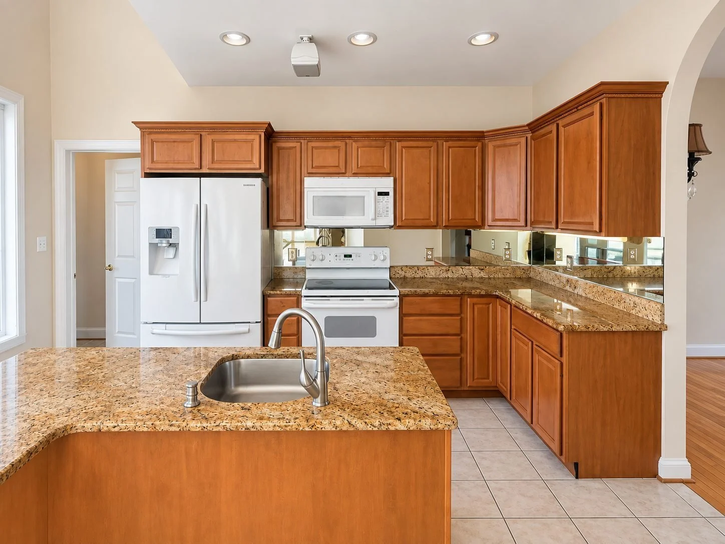 Kitchen before renovation, with cherry cabinets, granite counters, mirrored backsplash and tile floor
