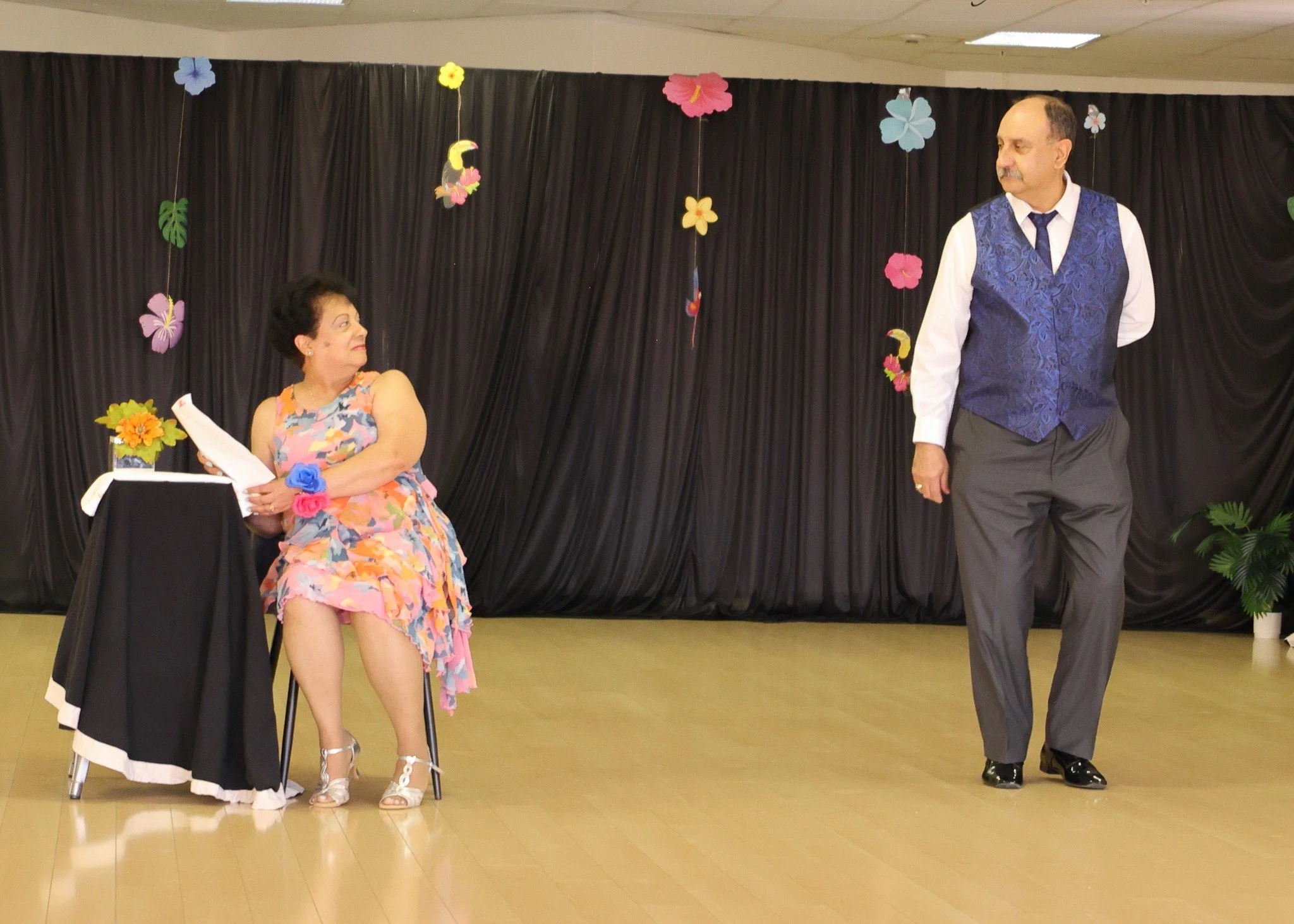 A seated performer and her dance partner share a theatrical showcase moment