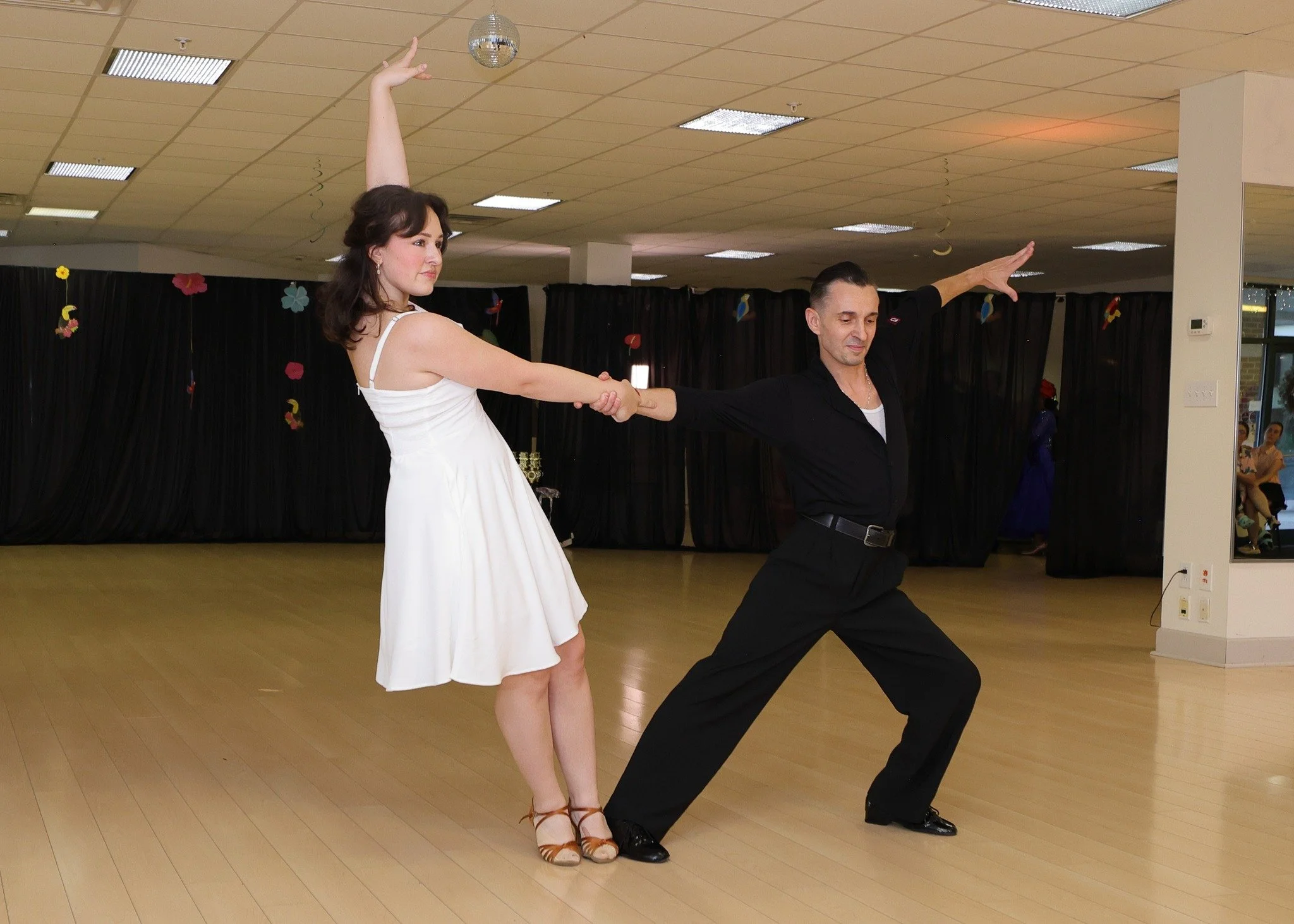 A dancer in white reaches toward her partner during a showcase routine