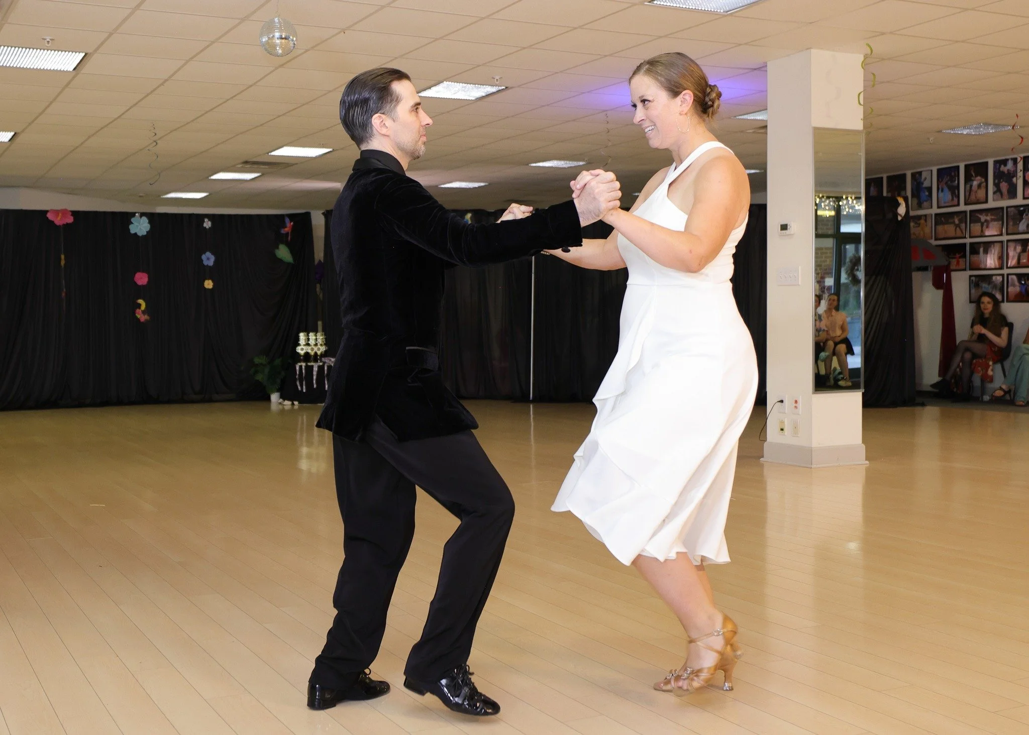 A ballroom couple dances in hold, with the performer wearing a white dress