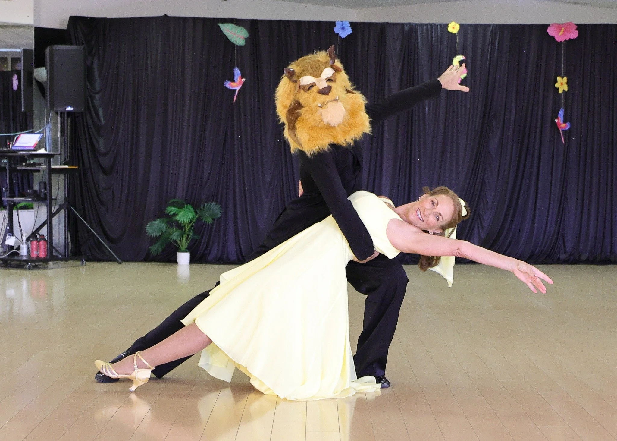 A performer in a pale yellow dress holds a dramatic dip with her dance partner