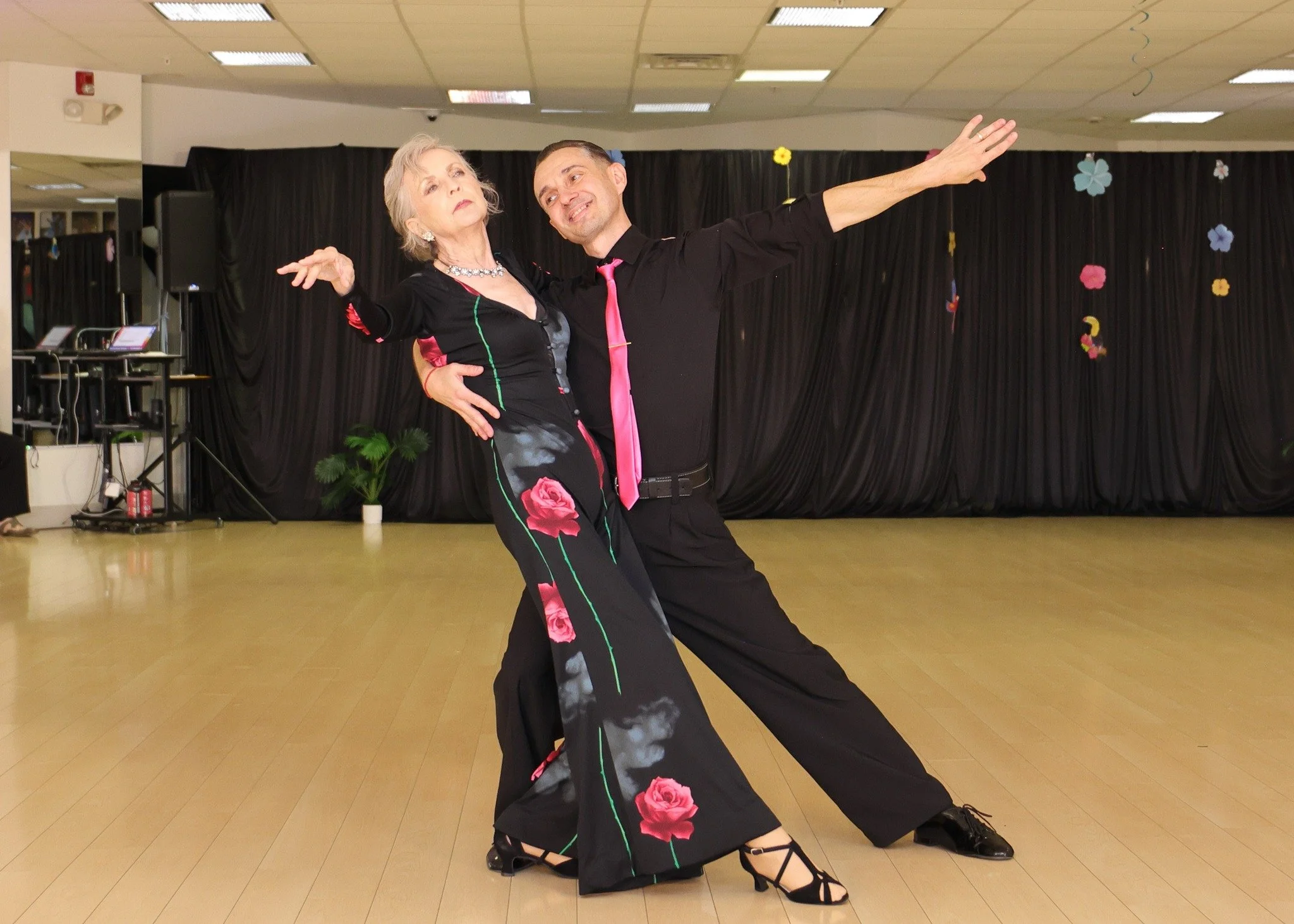A ballroom couple in black and pink extends into a dramatic showcase pose